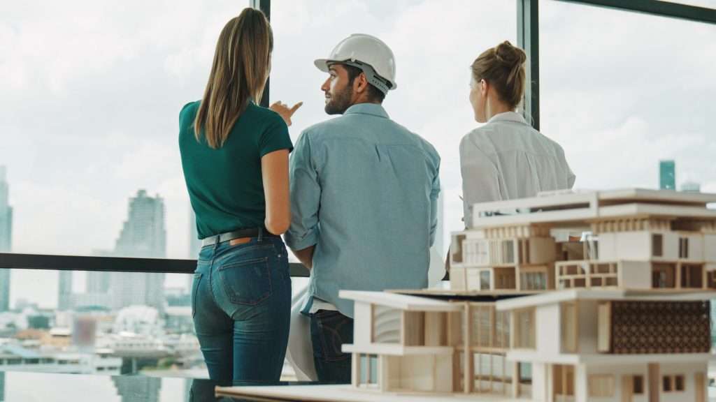 Group of caucasian engineer pointing at skyscraper. Back view. Tracery